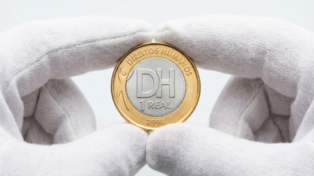 Close macro profissional da moeda de Direitos Humanos de 1998 sendo segurada por luvas brancas de numismática