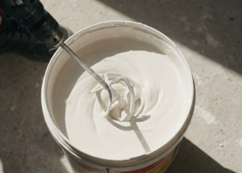 Mistura de massa corrida com corante sendo preparada em balde para pintura residencial