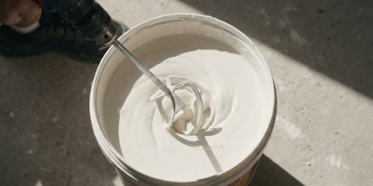 Mistura de massa corrida com corante sendo preparada em balde para pintura residencial