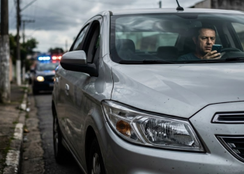 Motorista apreensivo em carro de 2016 com luzes de blitz ao fundo