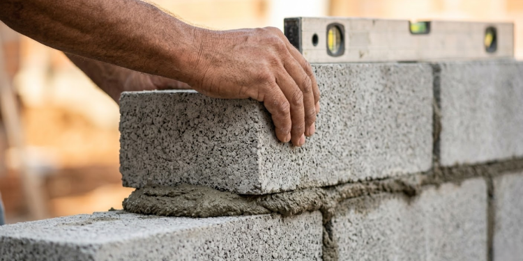 Mãos de um pedreiro assentando blocos de concreto com precisão.