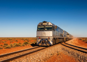 Trem prateado cruzando a maior reta do mundo na planície deserta sob a luz do pôr do sol.