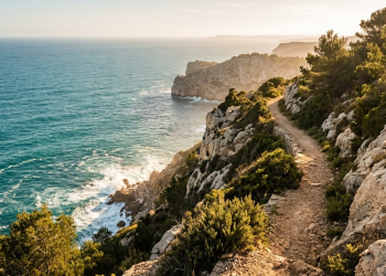 Trilho de terra batida contornando falésias sobre o mar azul.
