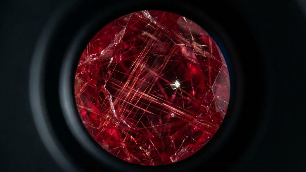 Especialista utiliza lupa triplet para analisar a pureza de uma esmeralda bruta sobre mesa de luz