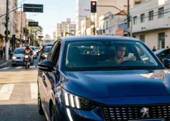 Avaliar o Peugeot 208 1.0 no trânsito diário revela um conflito interessante entre o visual arrojado externo e a pura vocação urbana interna. A carroceria esculpida sugere esportividade imediata, mas o verdadeiro ganho para o motorista está na economia constante de combustível. Como o desenho da cabine altera a percepção de espaço? Sentar no banco do motorista exige uma pequena adaptação inicial devido ao volante de dimensões reduzidas posicionado abaixo do quadro de instrumentos digital. Esse arranjo visual muda totalmente a perspectiva de quem conduz, criando uma sensação de amplitude rara em veículos compactos projetados para ruas estreitas. Em vez de adotar um interior conservador para baratear custos, a fabricante concentrou recursos em elementos visuais de impacto tátil para afastar a imagem de carro popular de entrada. A seguir, os pontos que realmente importam: Materiais suaves ao toque no painel frontal reduzem significativamente a percepção de plástico rígido. Tela multimídia inclinada para o condutor diminui reflexos incômodos em dias muito ensolarados. Teclas centrais em formato de atalhos de aviação facilitam o acionamento de comandos sem olhar. Posição de dirigir mais esportiva diminui a fadiga nas costas durante trajetos longos na cidade. Volante achatado nas extremidades libera mais espaço real para a movimentação das pernas do condutor. Por que a escolha mecânica privilegia a rotina na cidade? O conjunto motriz adota uma arquitetura de três cilindros focada na entrega de força em rotações iniciais. Essa característica mecânica elimina a necessidade de esticar as marchas em semáforos, garantindo saídas ágeis e bastante progressivas mesmo com o ar-condicionado operando em capacidade máxima. O projeto obteve classificação de excelência no programa nacional de eficiência energética devido à sua calibração focada na redução de gasto de combustível nas vias urbanas. Na tabela abaixo, um resumo comparativo: Ambiente de rodagemResposta do motorImpacto no consumoTrânsito pesado (anda e para)Entrega rápida de força em baixaRedução severa de desperdício de combustívelAcelerações contínuas em subidasManutenção de rotação estávelMaior eficiência térmica durante o esforçoVelocidade de cruzeiro constanteRotação estabilizada e silenciosaAutonomia estendida entre abastecimentos Onde o refinamento esconde suas limitações reais? Toda essa sofisticação estética e eficiência urbana cobram um preço imediato no aproveitamento do espaço no banco traseiro. Passageiros mais altos encontram grande dificuldade para acomodar as pernas com conforto, um sacrifício físico comum quando os projetistas priorizam o formato aerodinâmico externo em vez da carroceria quadrada. A suspensão dianteira, embora muito eficiente para filtrar o asfalto levemente irregular, transmite batidas secas quando o veículo cai em buracos profundos e inesperados. Segundo os princípios da dinâmica de veículos, ajustar molas para garantir estabilidade direcional em curvas sempre acaba penalizando a maciez geral. Para qual perfil essa proposta faz sentido prático? O pacote entregue pela marca francesa filtra o mercado de forma explícita, afastando motoristas que precisam de espaço familiar abundante para focar em quem roda a maior parte do tempo sozinho ou em dupla. A cabine moderna funciona como uma forte compensação psicológica para o volume menor. Trocar a área do banco traseiro por uma experiência de condução mais silenciosa e visualmente rica acaba recompensando o usuário estritamente urbano. O carro entrega a forte sensação de pertencer a uma categoria superior, transformando o trajeto rotineiro em um momento de isolamento muito confortável no asfalto.