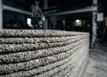Braços robóticos industriais que depositam cordões contínuos de argamassa de alta viscosidade, erguendo a estrutura de uma casa em menos de 48 horas com precisão milimétrica e resistência mecânica superior à do bloco de concreto comum