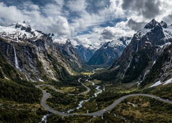 Com túneis escavados na rocha sólida e paredões com cachoeiras, a estrada desce as montanhas neozelandesas até o espetacular fiorde de Milford