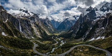 Com túneis escavados na rocha sólida e paredões com cachoeiras, a estrada desce as montanhas neozelandesas até o espetacular fiorde de Milford